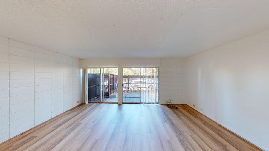 A room with wooden floors and white walls with a doorway leading to a balcony.